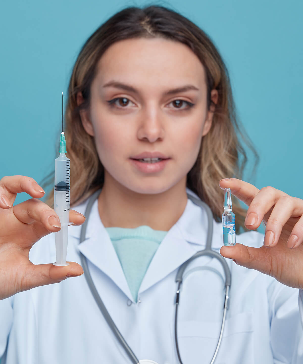 close-up-view-confident-young-female-doctor-wearing-medical-robe-stethoscope-around-neck-stretching-out-syringe-ampoule-towards-camera